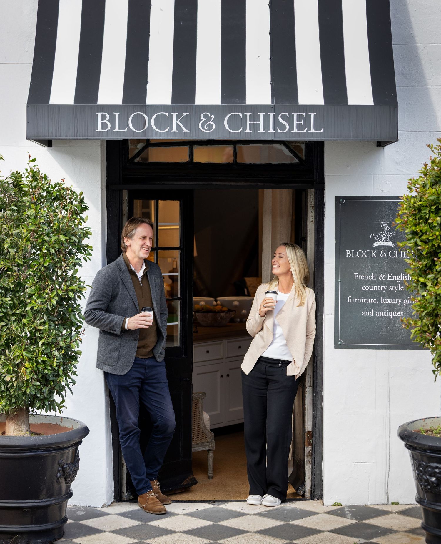 Two people having coffee outside Block & Chisel store entrance with black and white striped awning.