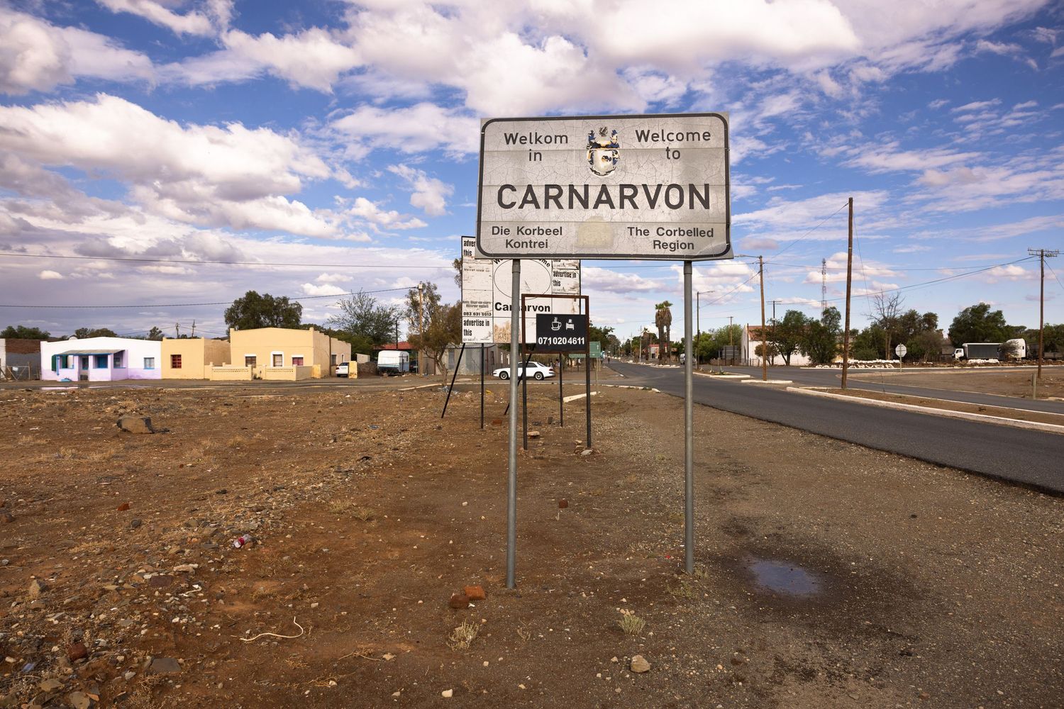 Road signs and buildings in remote desert town under blue sky.