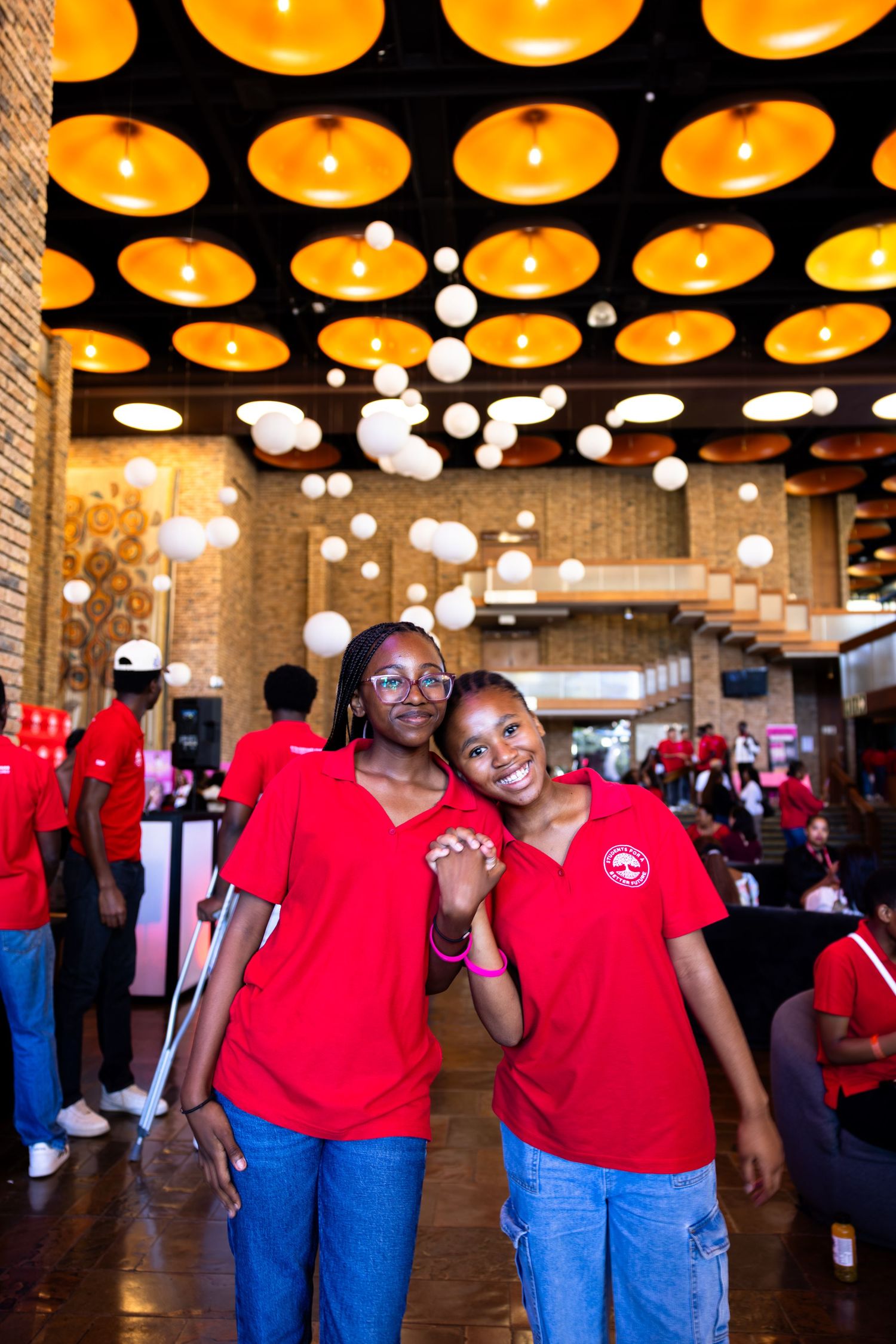 Group wearing matching red shirts and jeans standing under decorative yellow ceiling lights.