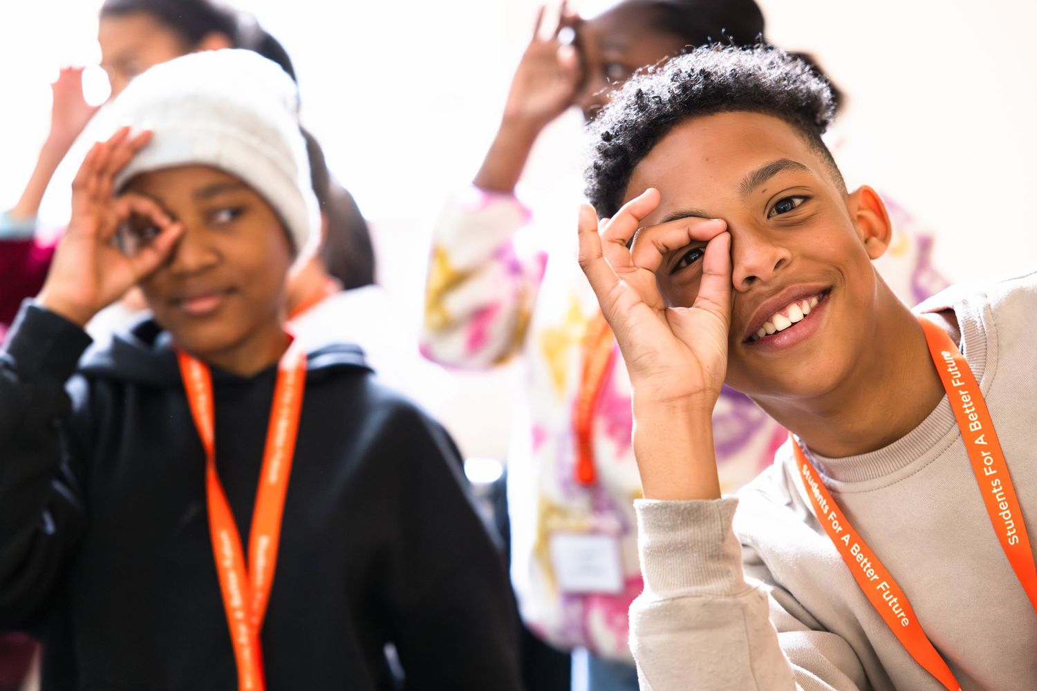 Students wearing orange lanyards smile and pose playfully during a school event.