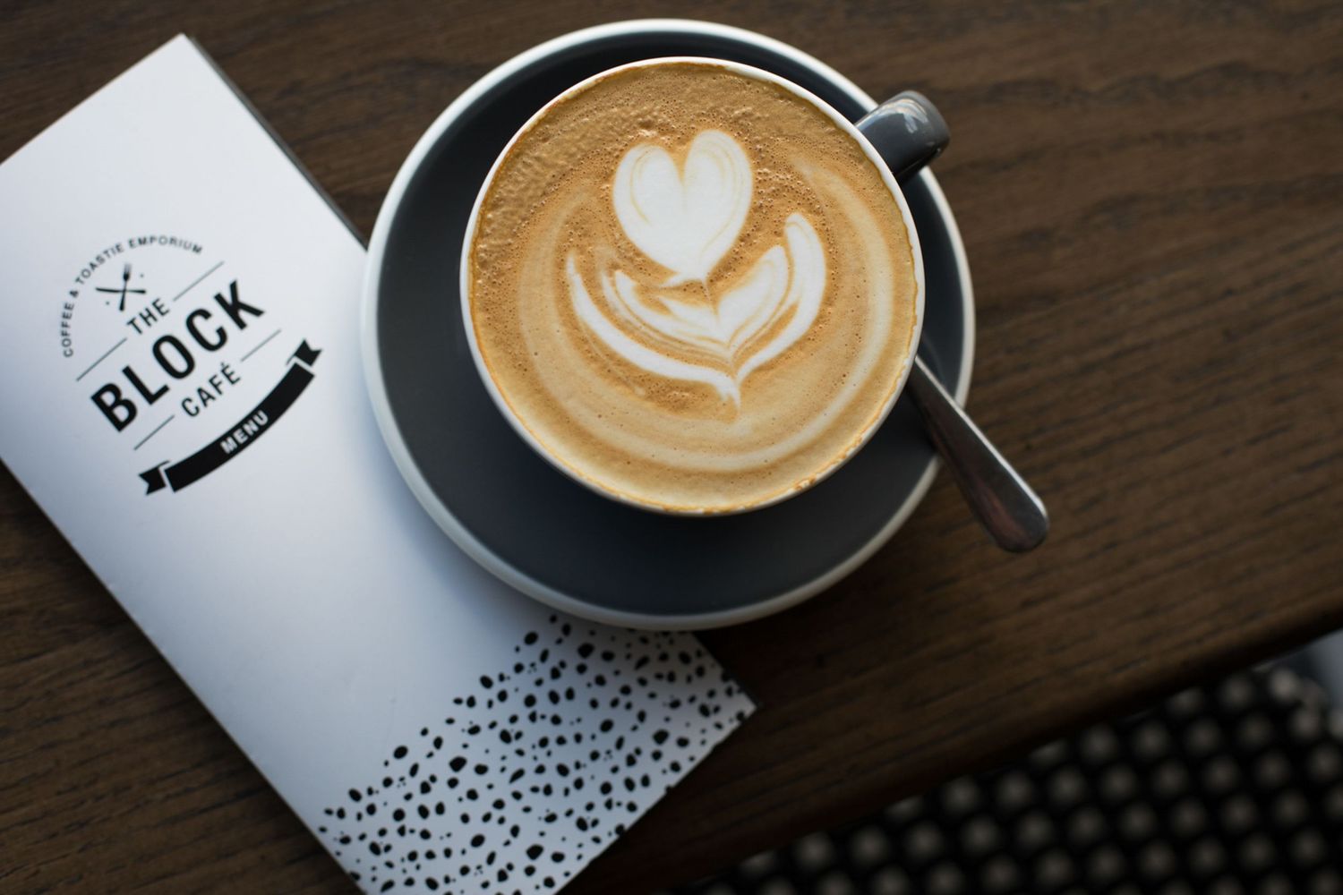 Latte art in coffee cups with Block Cafe branded materials on wooden table.
