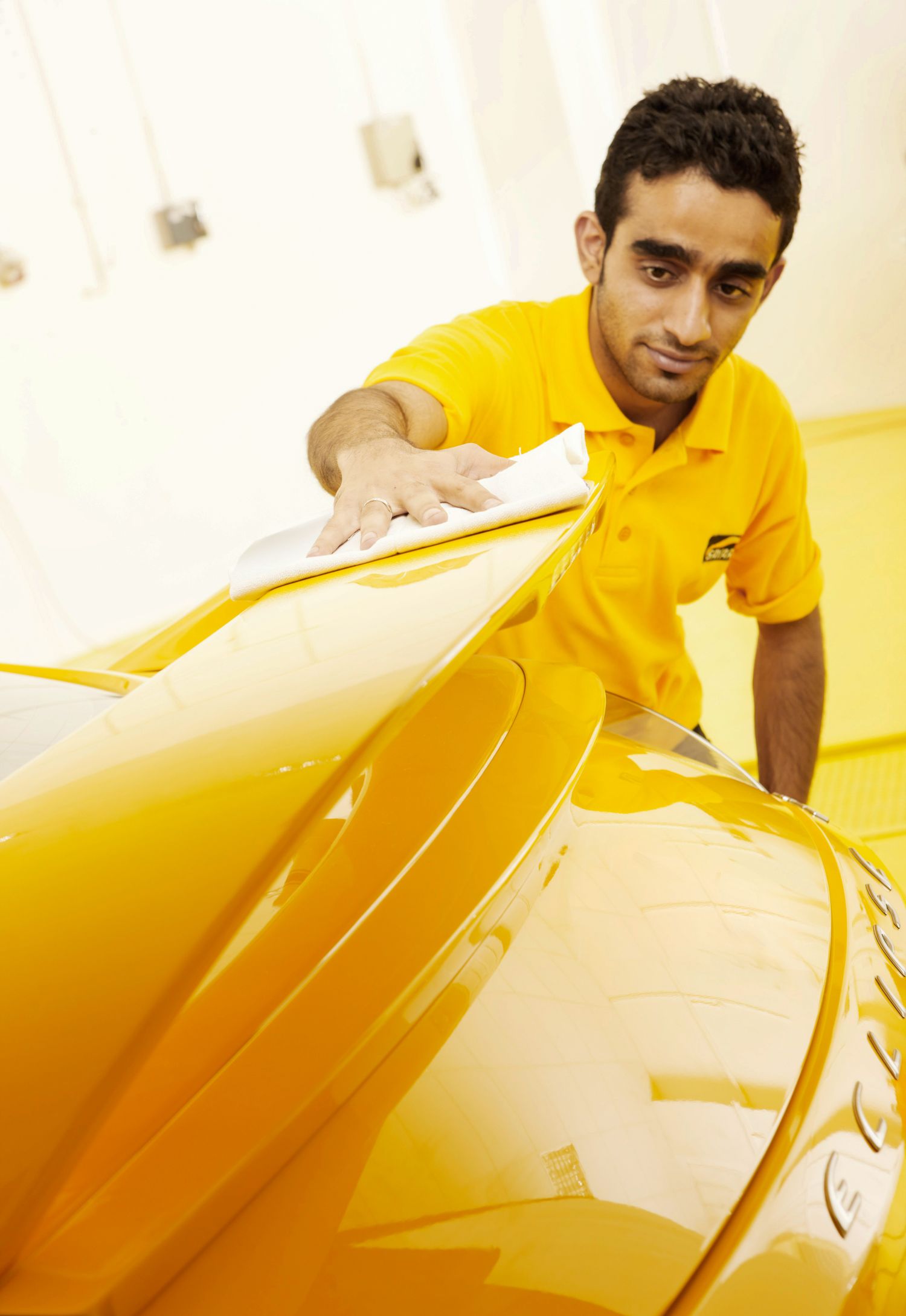 Auto detailer in yellow uniform carefully examining yellow car's surface finish.