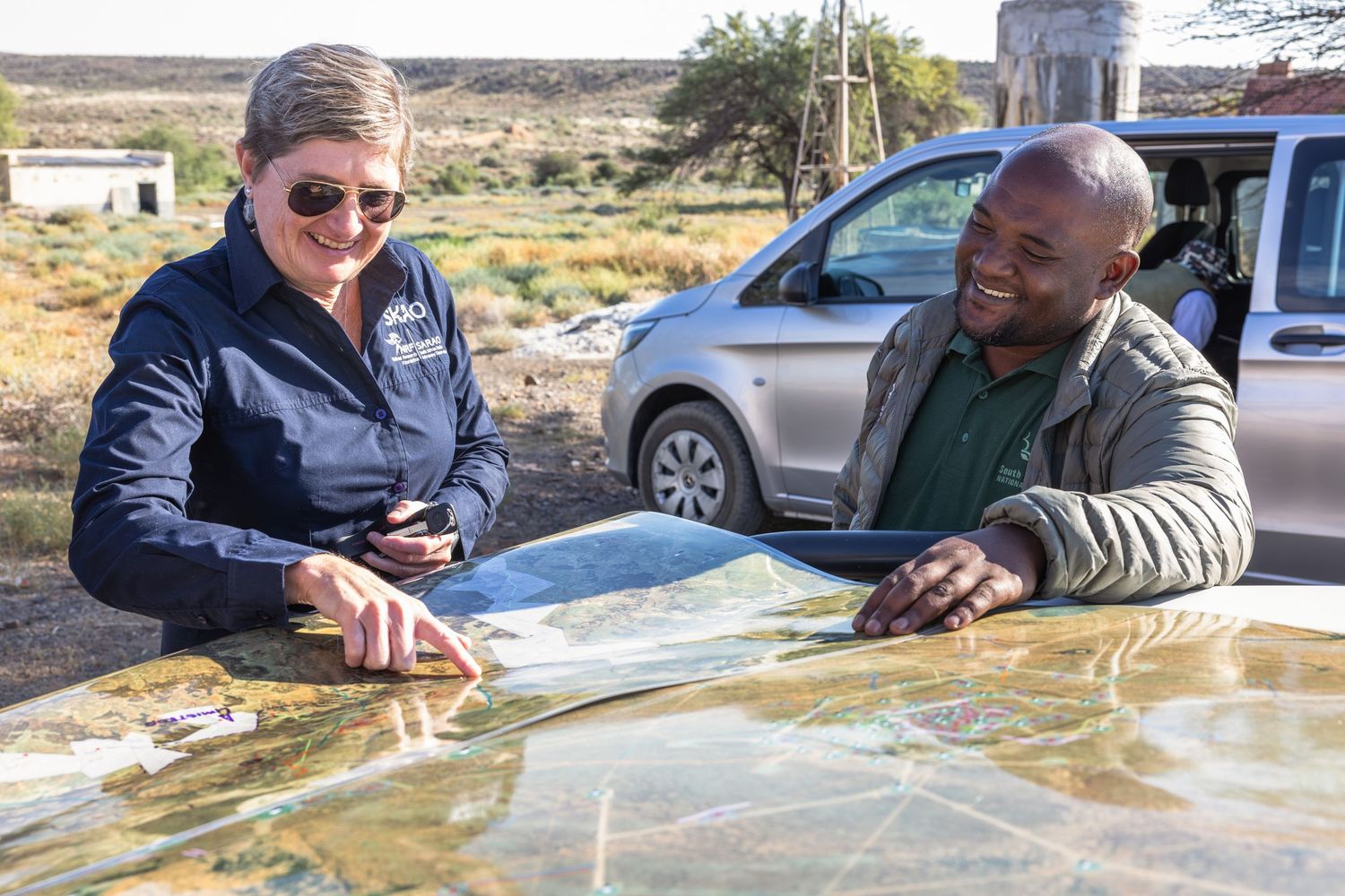 Team reviewing maps and plans on vehicle hood in desert setting.