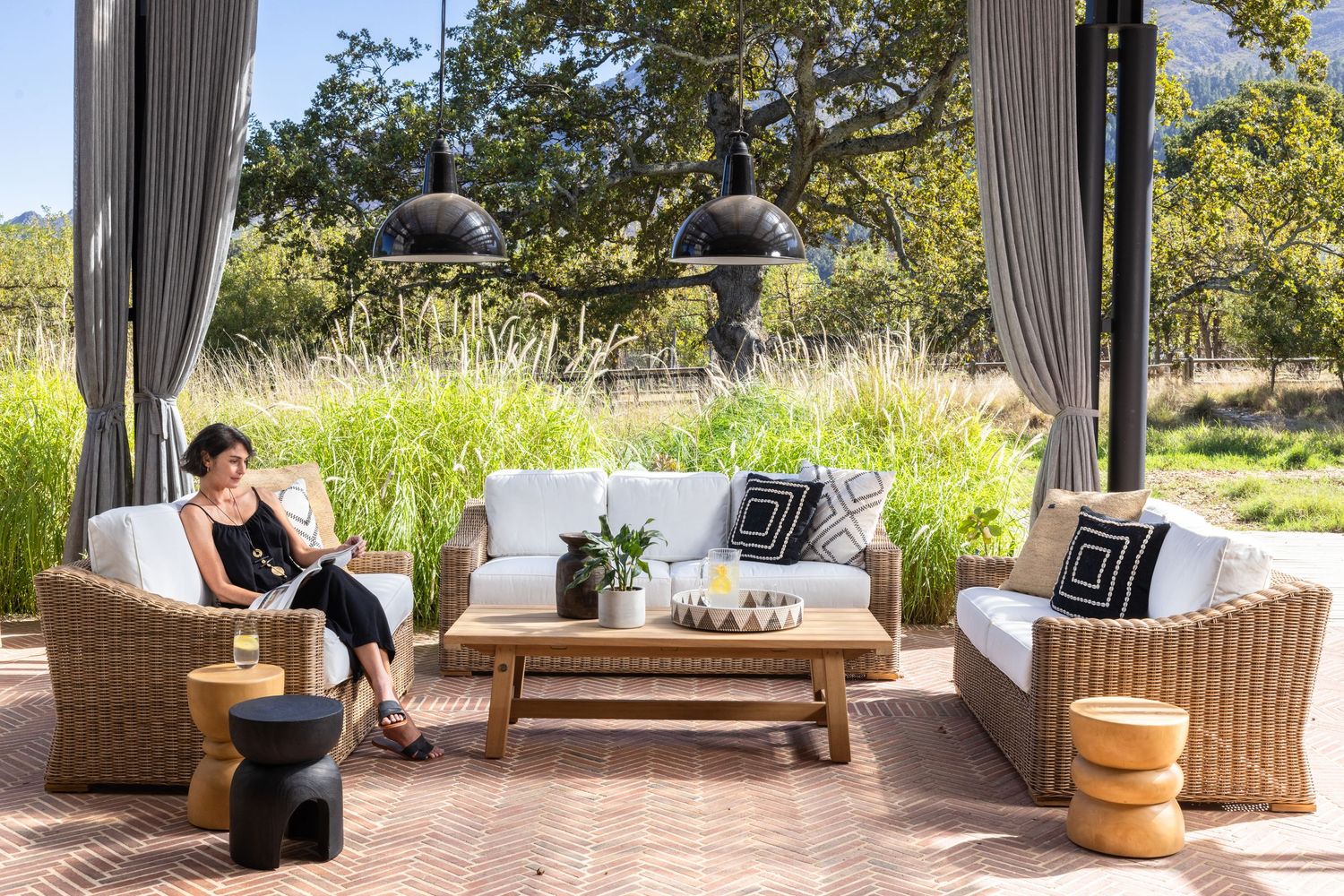 Luxurious outdoor patio lounge area with wicker furniture and white cushions under a pergola in a garden setting.