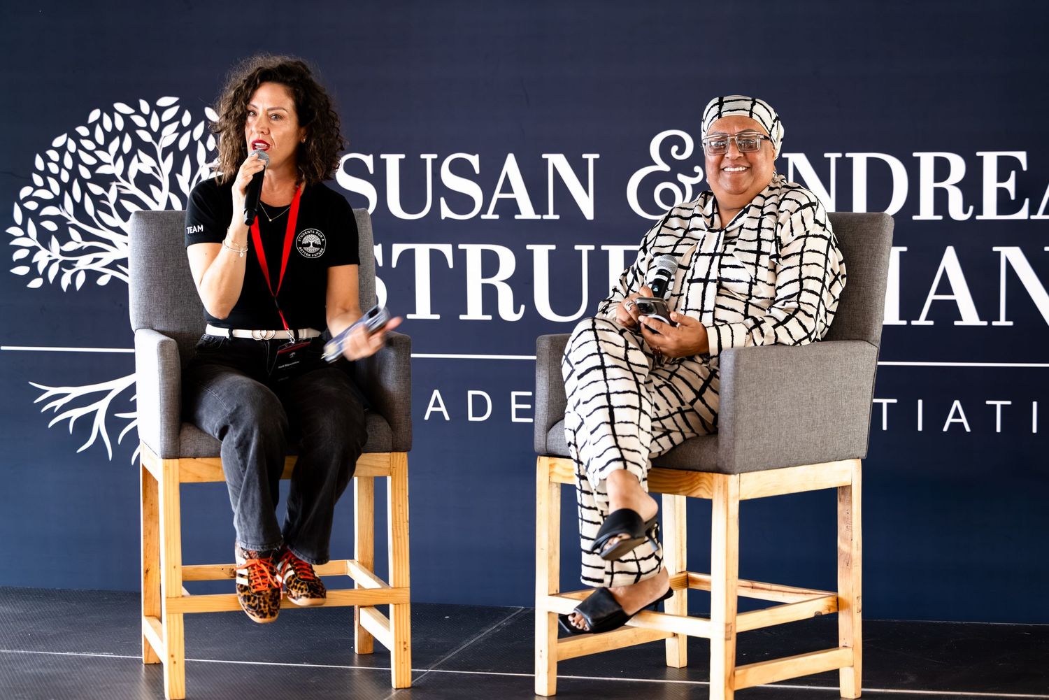 Two speakers participate in a panel discussion at a branded conference event.