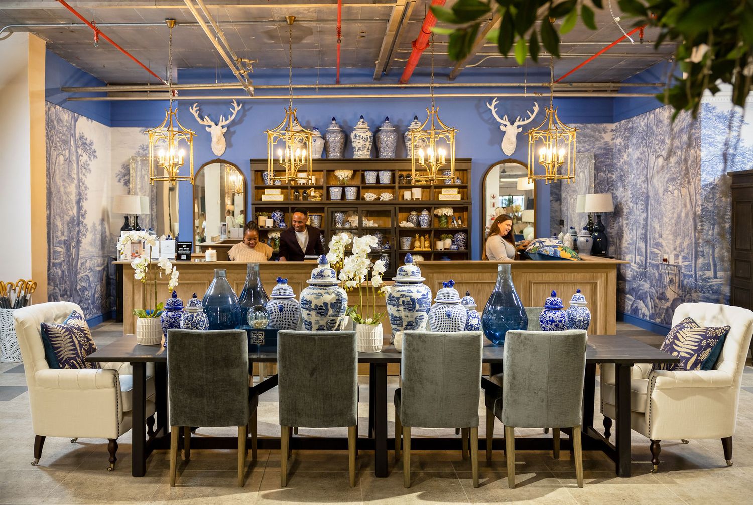 Elegant dining room display with blue wallpaper, deer head decor, and crystal chandelier in furniture showroom.