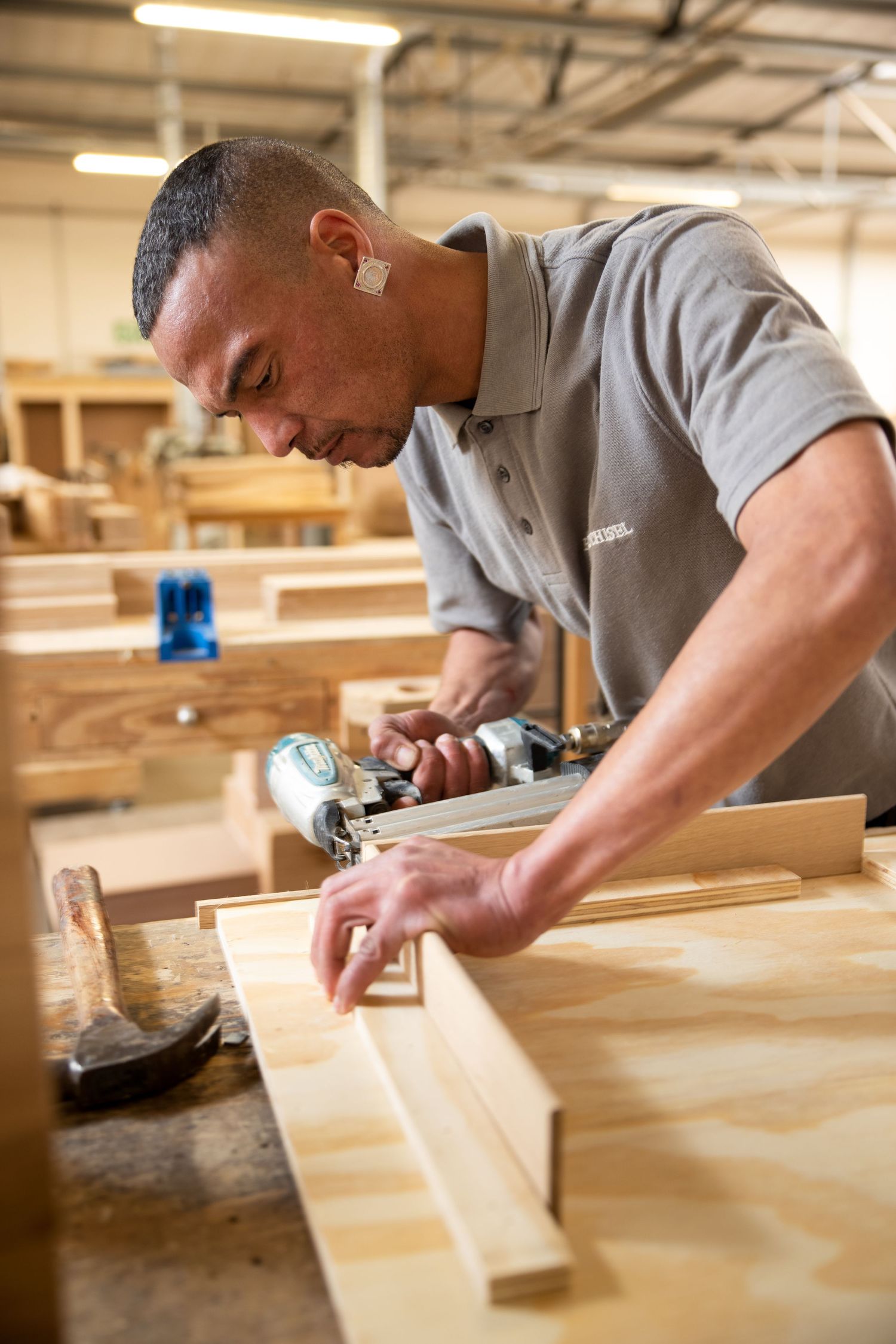 Craftsman working with precision on wooden furniture pieces in a bright workshop.