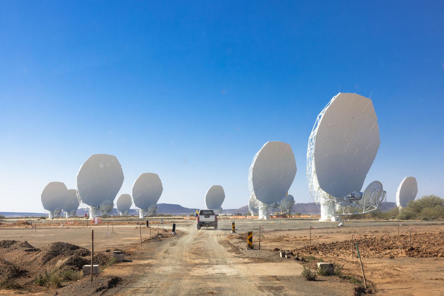 Array of large satellite dishes and dome structures at desert communications facility.