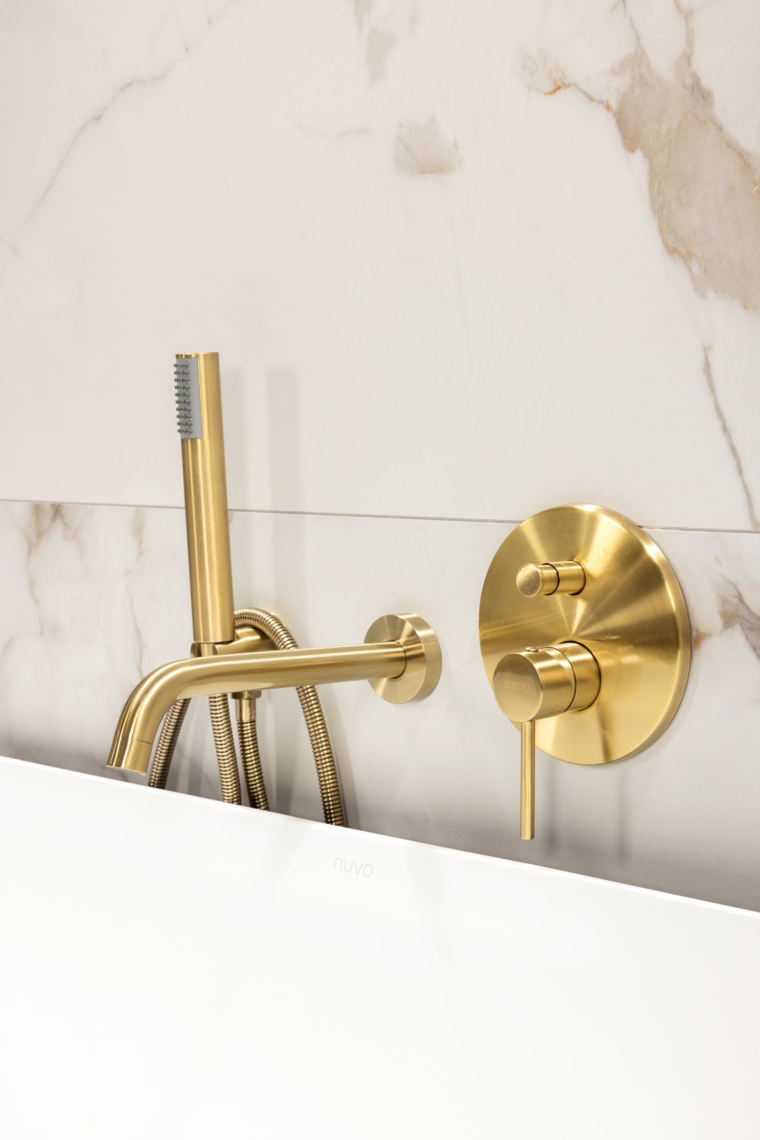 Gold brushed metal wall-mounted bathtub faucet against marble wall background.