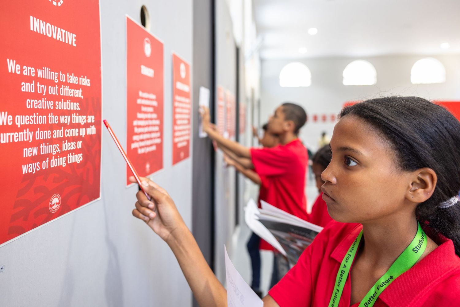 People in red shirts reading text on white walls in a modern office hallway.