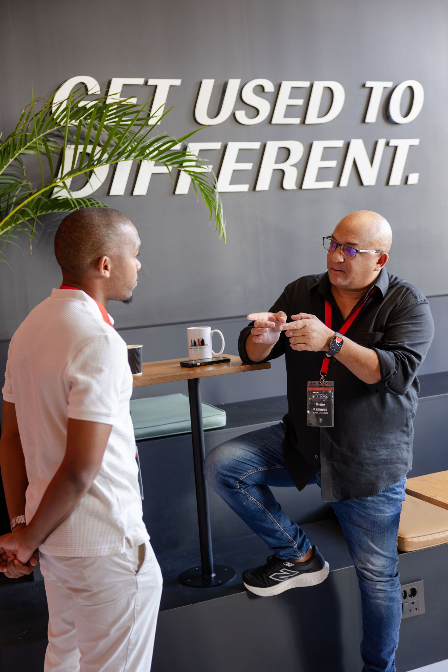People having informal conversations in a modern office space with text on wall.