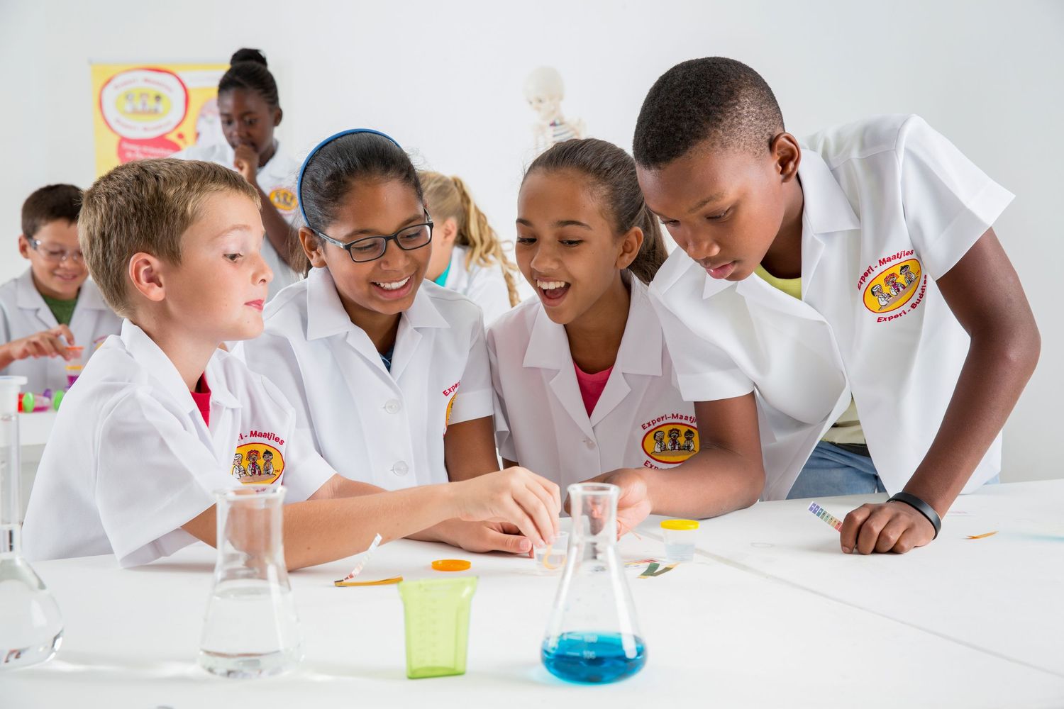 Students gather around a table examining colorful liquids during a science experiment.