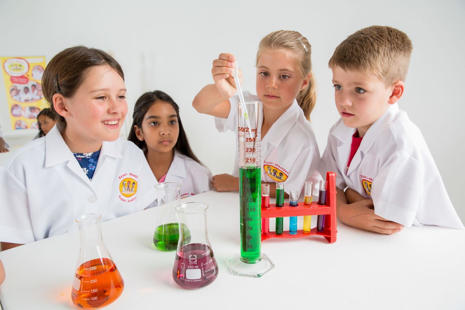 Students in white lab coats observing colorful chemical reactions in beakers during a science experiment.