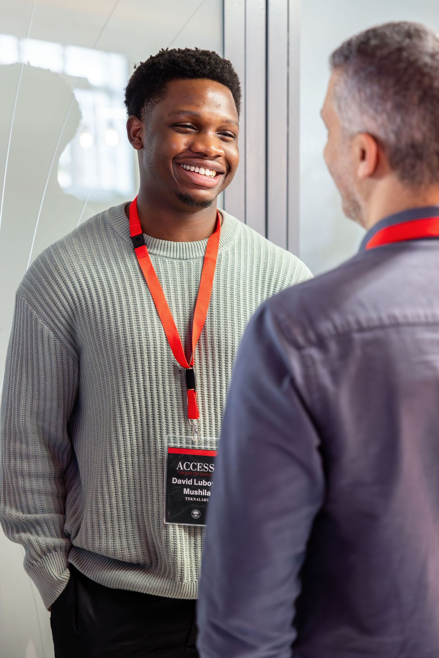 Professional conversation between two people wearing lanyards in an office environment with bright lighting.