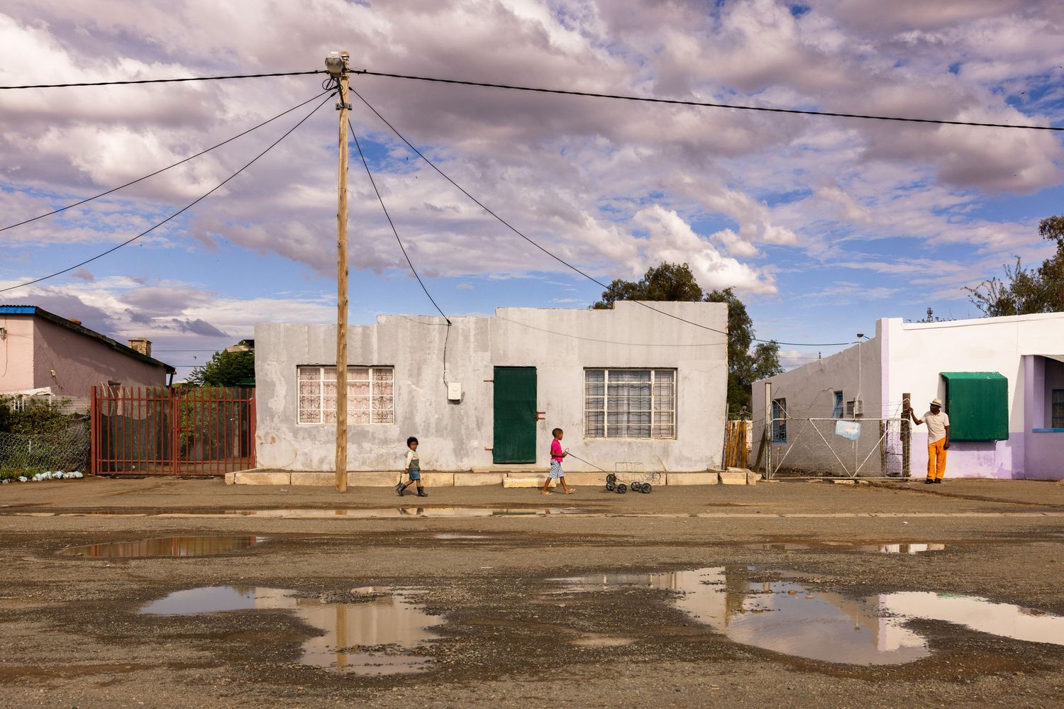 Panoramic view of a small rural town with simple buildings along dirt roads under a cloudy sky.