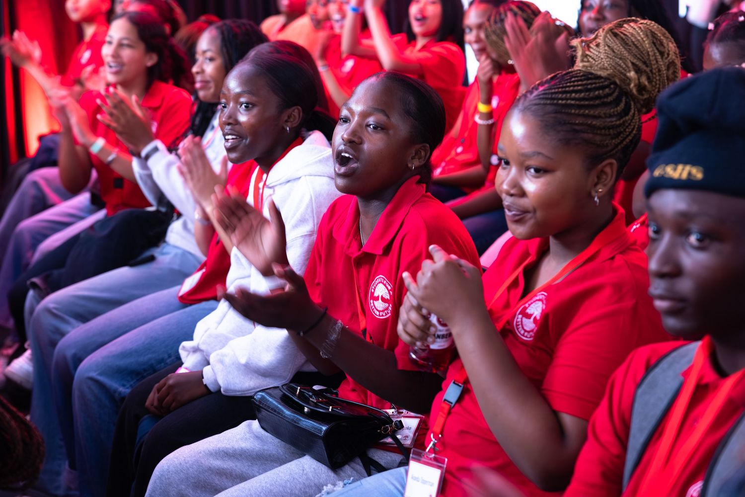 An engaged audience in red uniforms watches attentively during an indoor gathering.