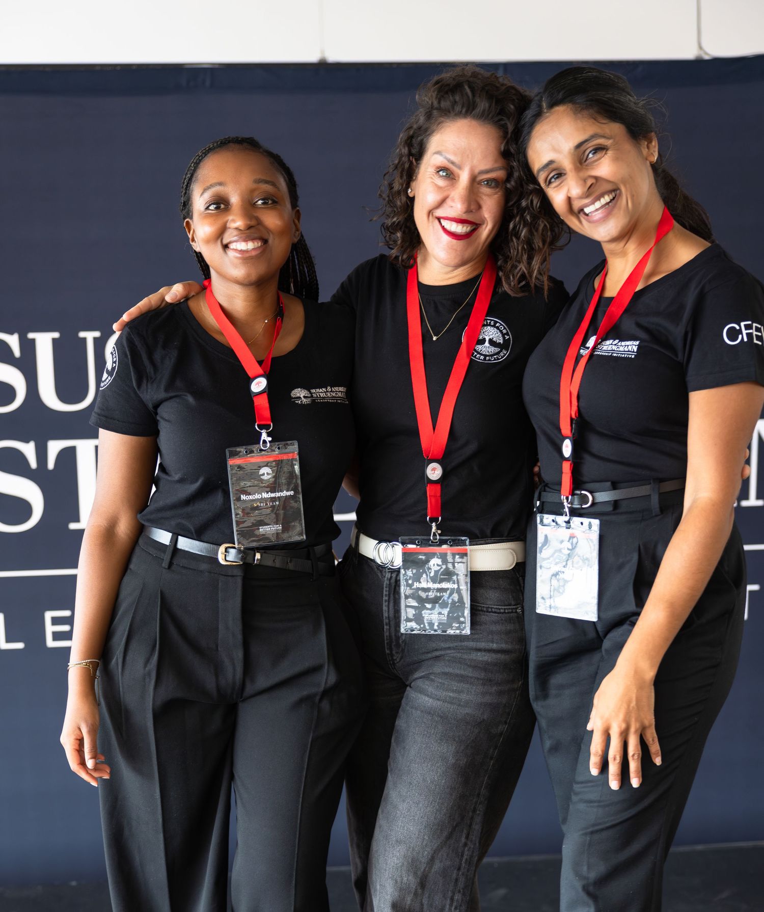 Three staff members wearing black uniforms and event badges smile together at a conference.