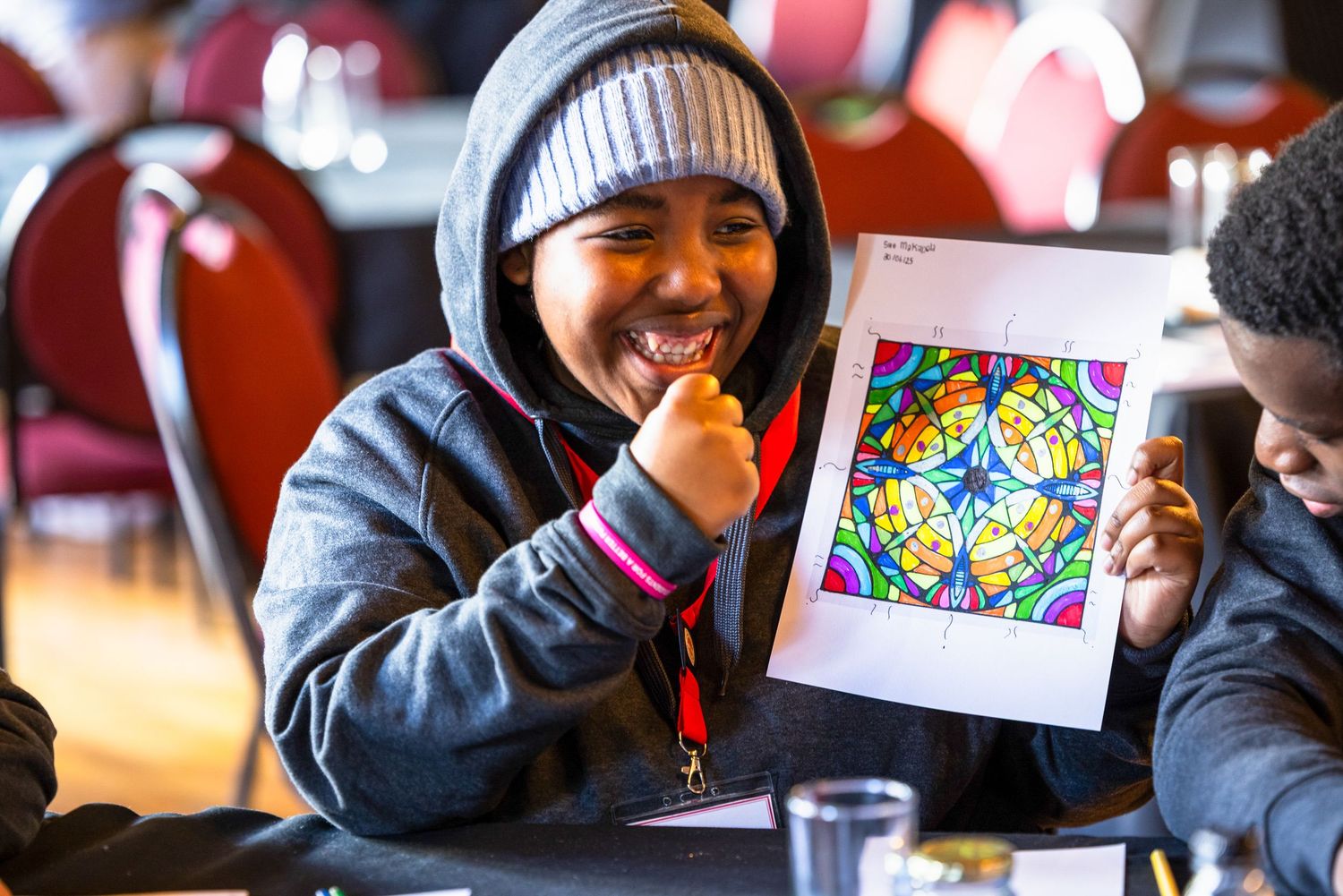 Student displaying colorful stained glass-style artwork during art class.