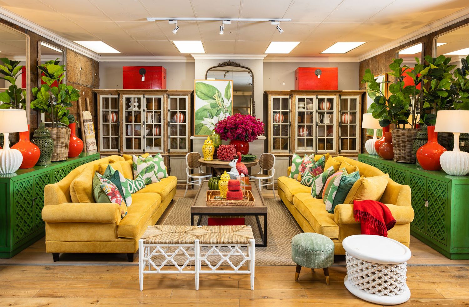 Vibrant yellow sofas with colorful pillows flank a glass coffee table in a room decorated with tropical plants.