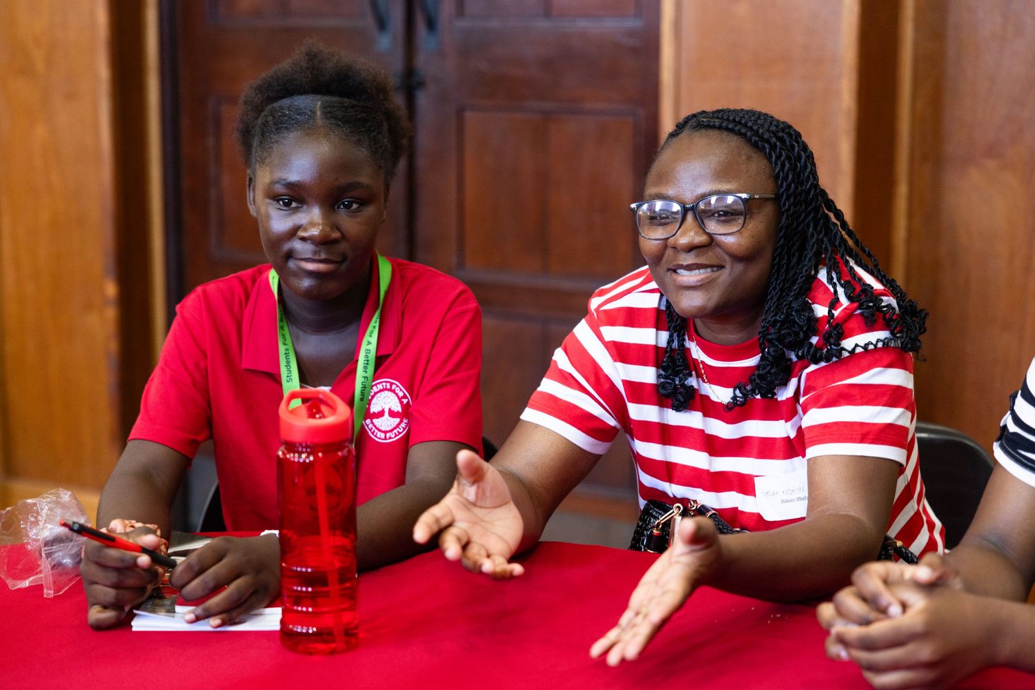 Students in red shirts sit together at tables during a group learning session.