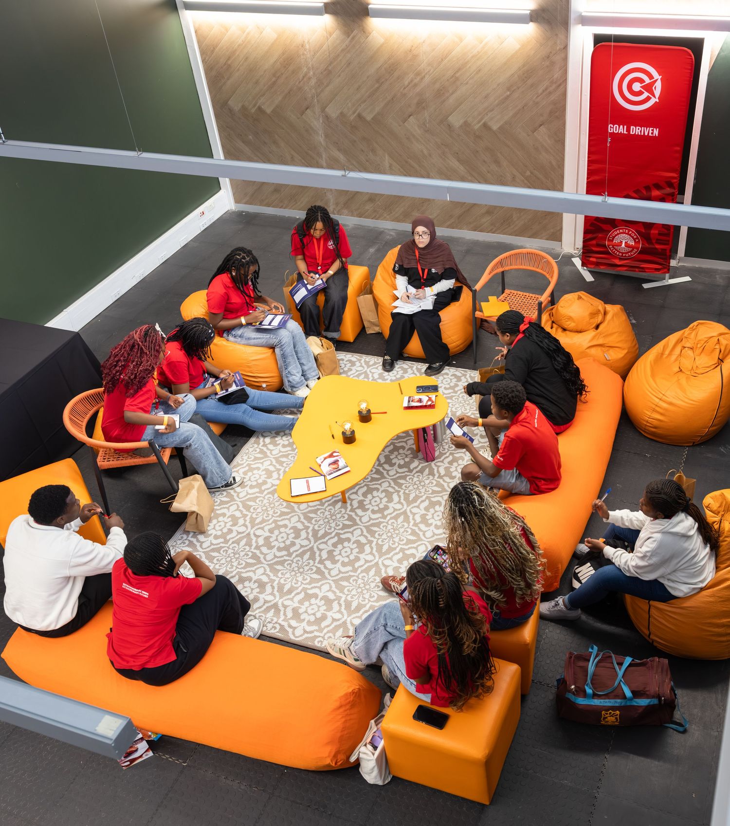 Students relax on orange bean bag chairs while working on laptops in a casual study space.