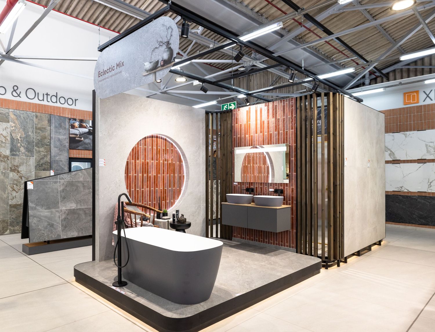 Contemporary bathroom vignette with dark freestanding tub and circular window display in a retail showroom setting.
