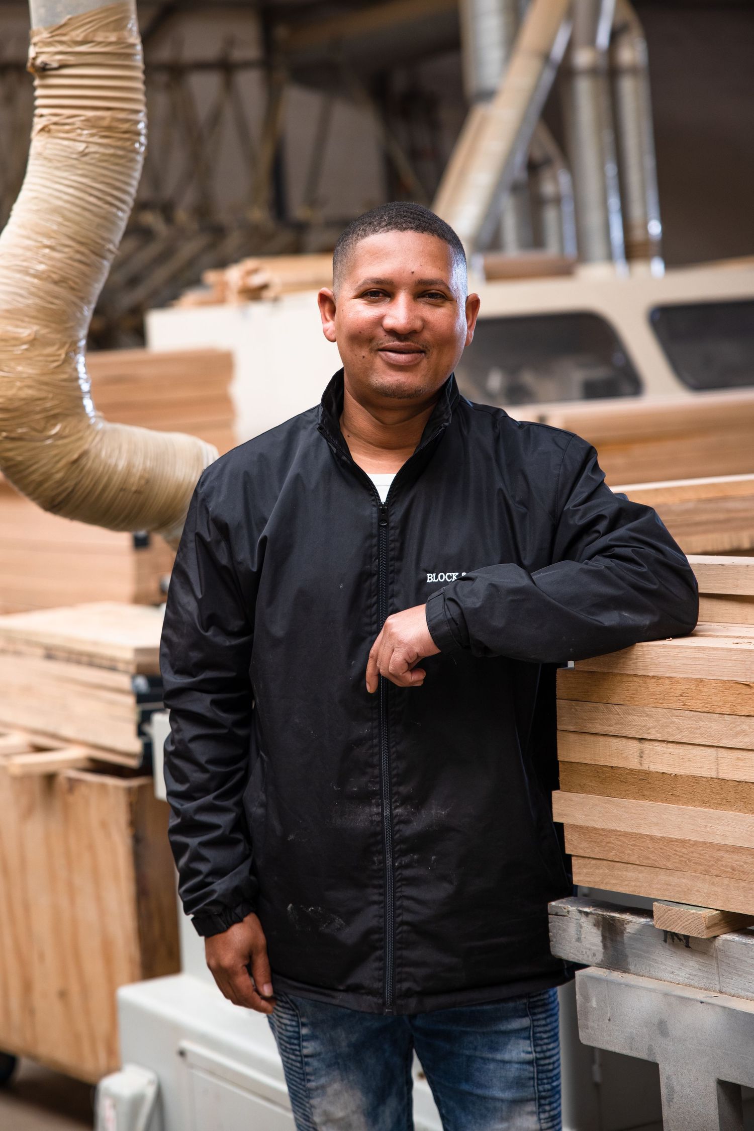 Craftsmen in black workwear inspect wooden materials in an industrial workspace.