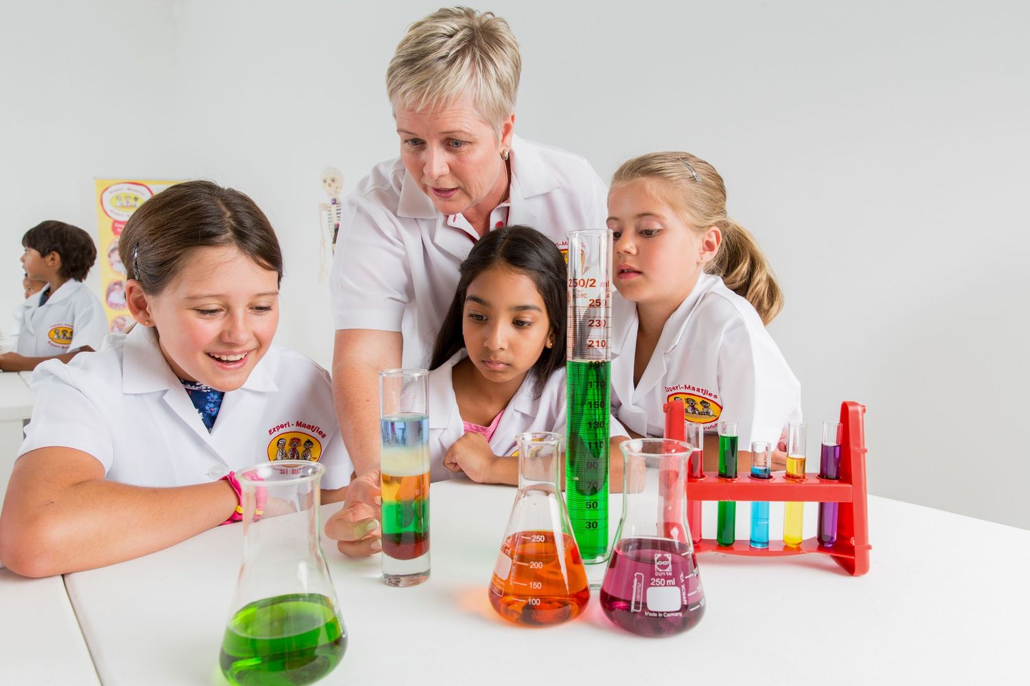 Students gather around table to observe colorful chemical reactions during science experiment.