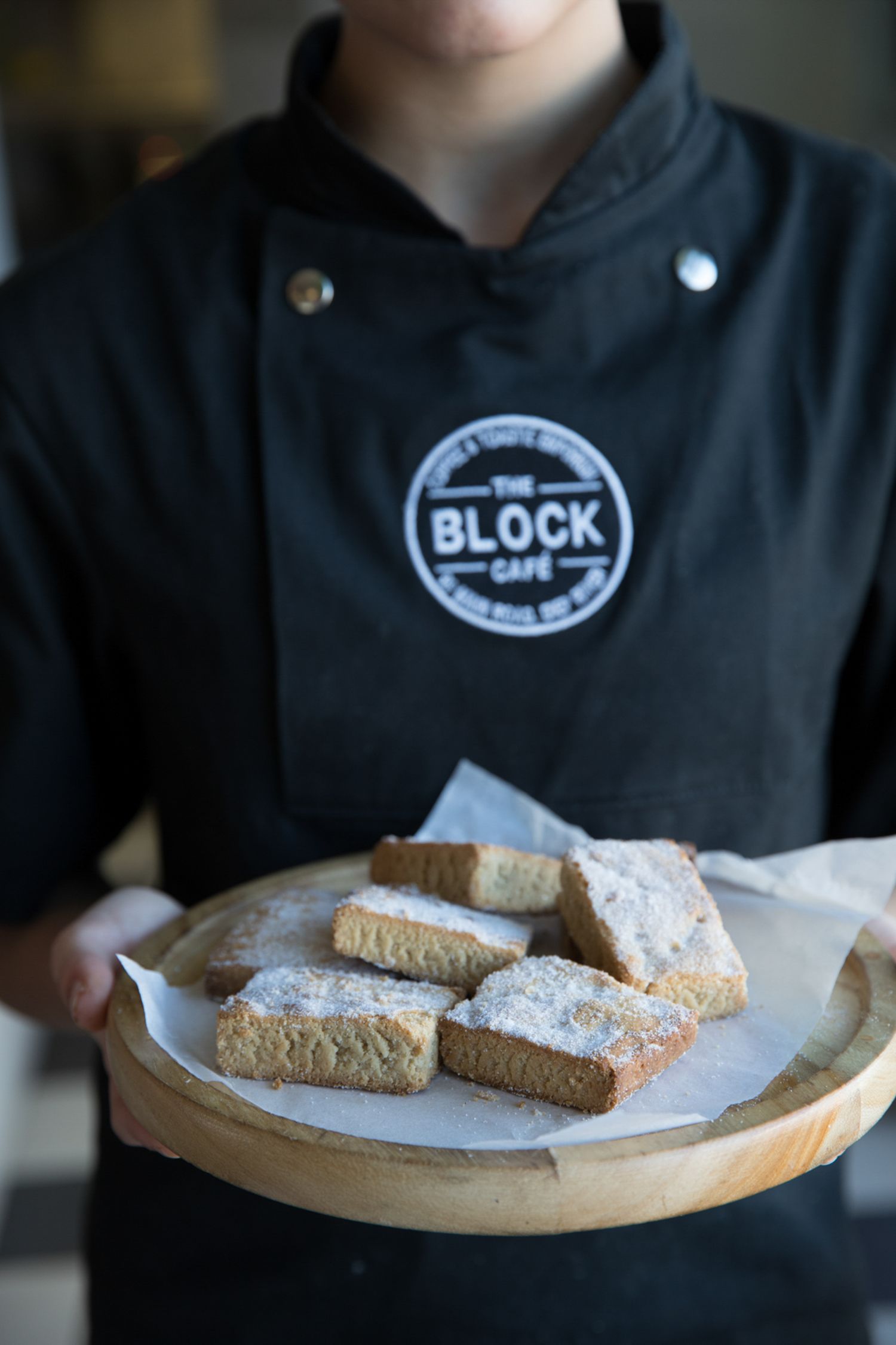 Freshly baked biscotti dusted with powdered sugar displayed on a round wooden serving board.