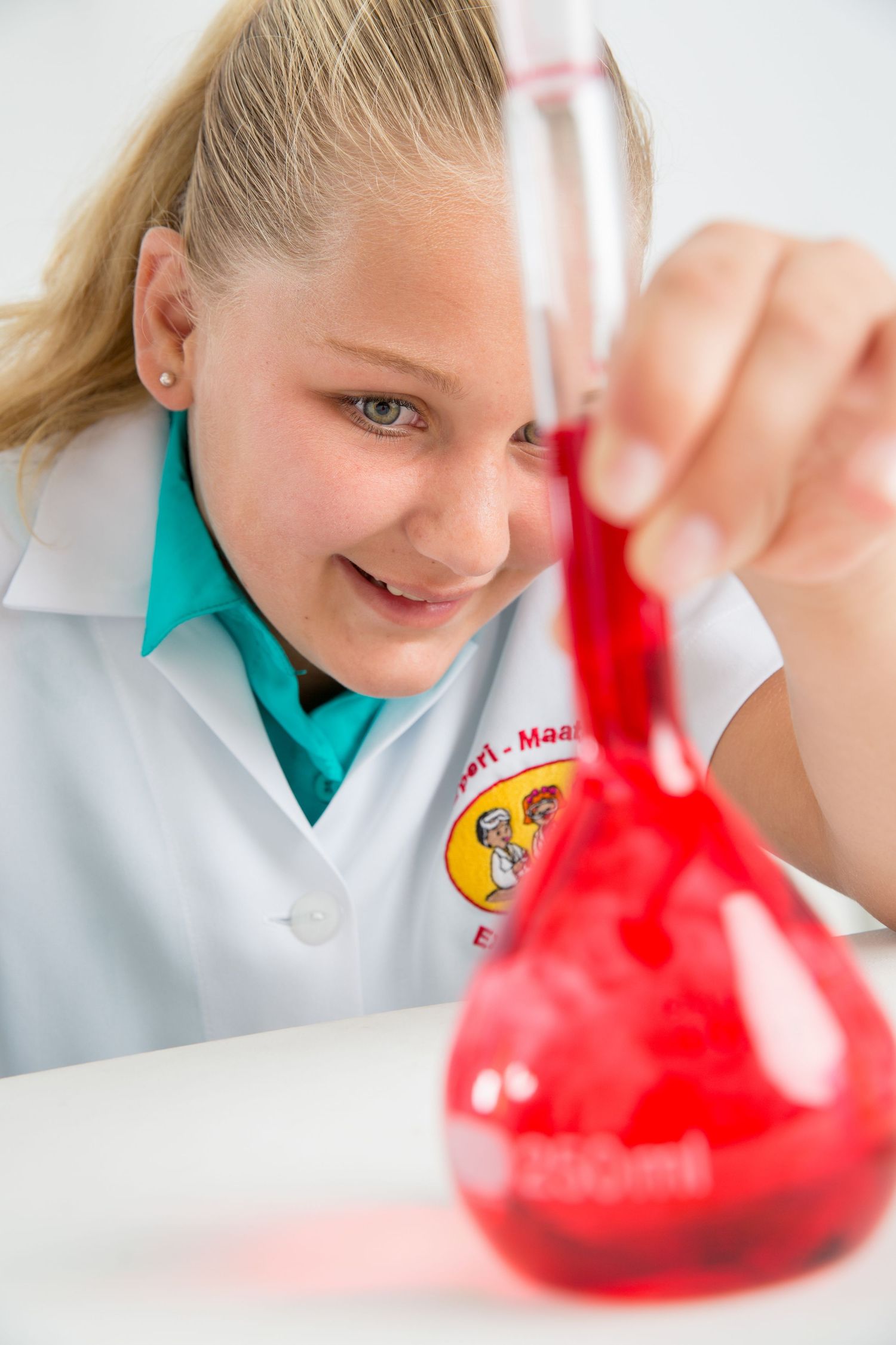 Student in a white lab coat examines a red liquid in a chemistry flask during a science experiment.