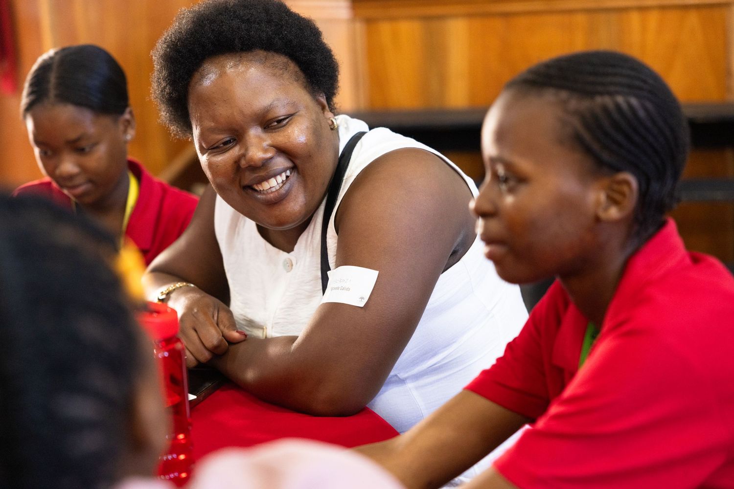 People in red shirts engage in group discussions at tables during a community gathering.