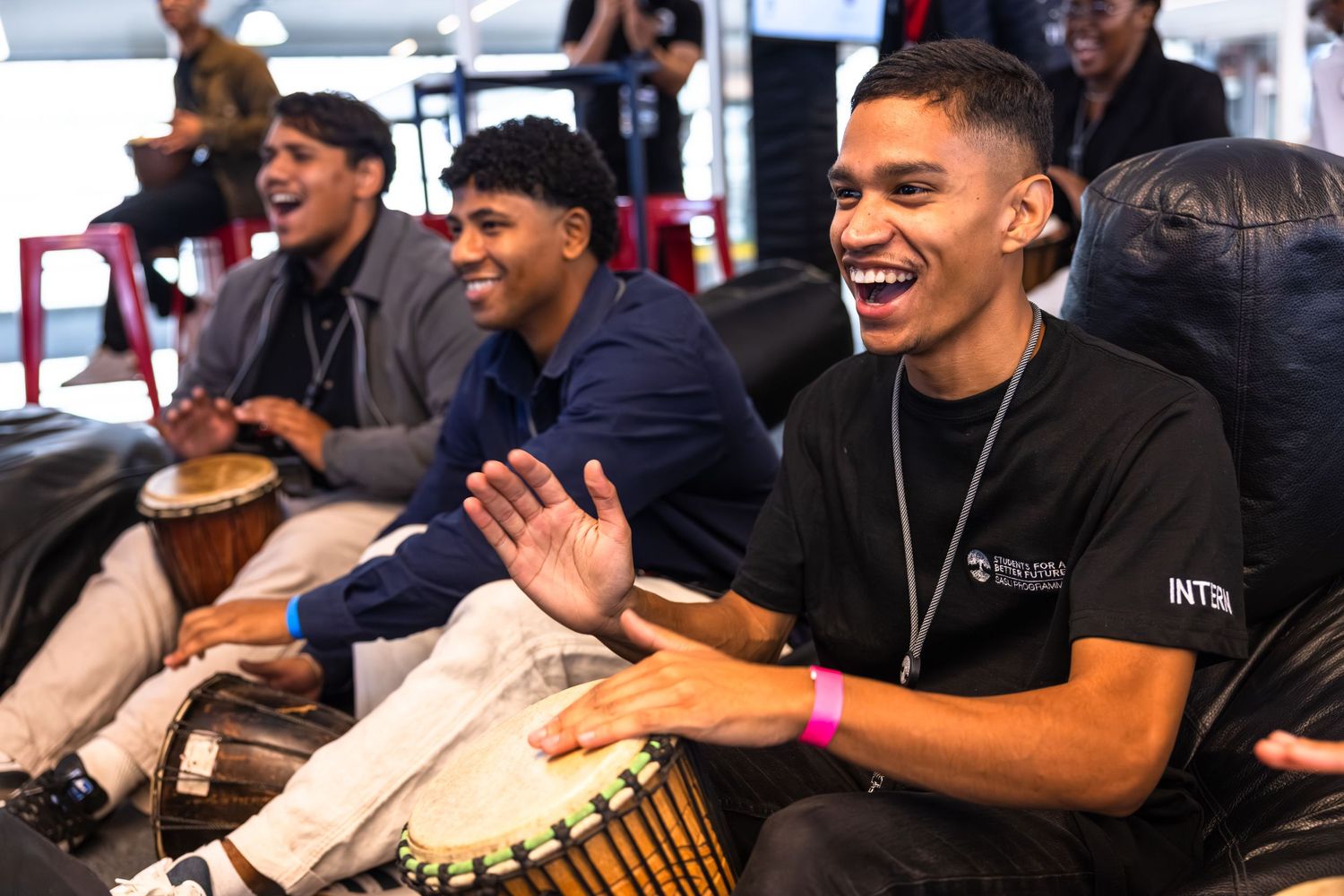 Musicians playing drums and percussion instruments while smiling and performing together.