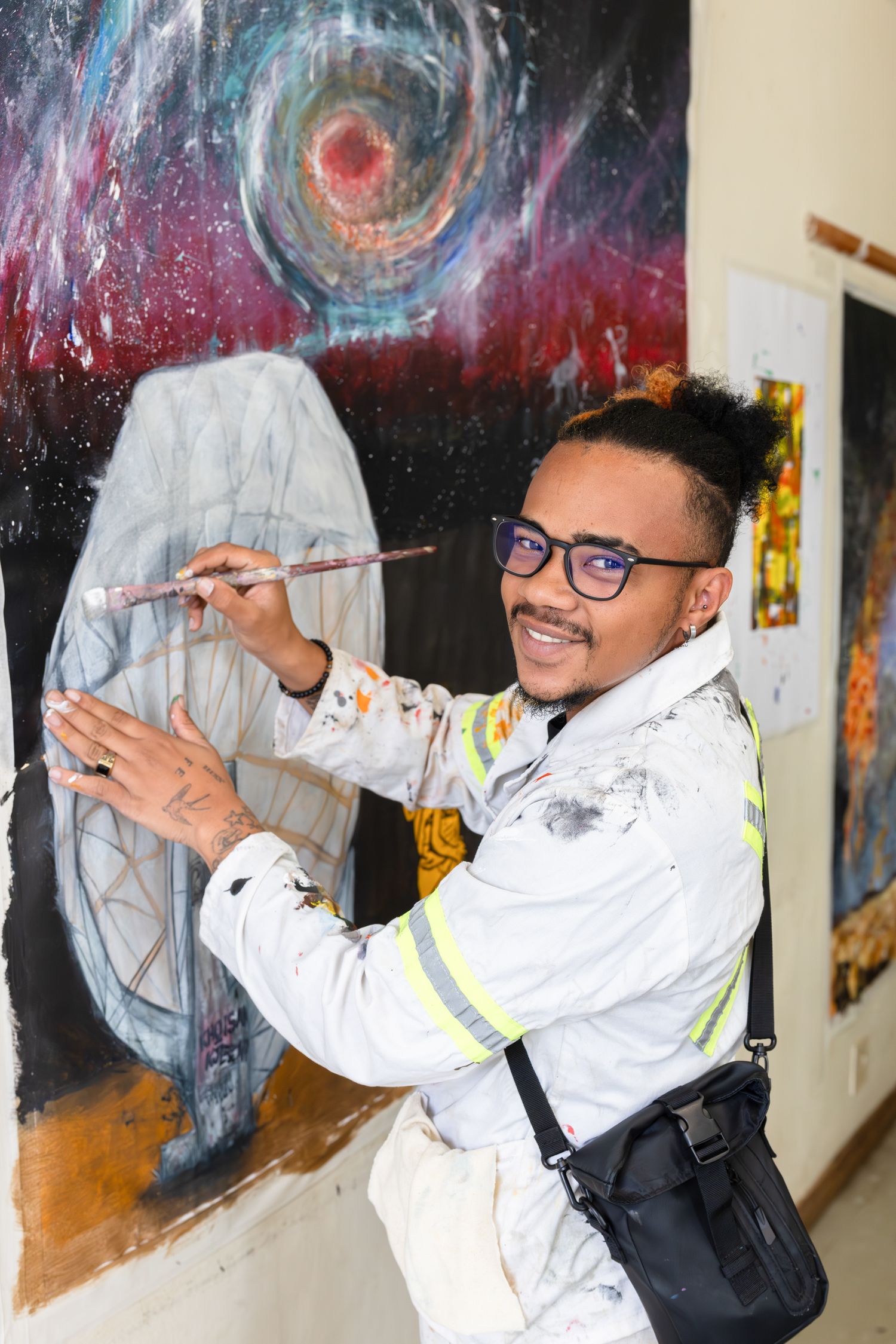 Artist in glasses painting on a cosmic-themed mural with swirling patterns.