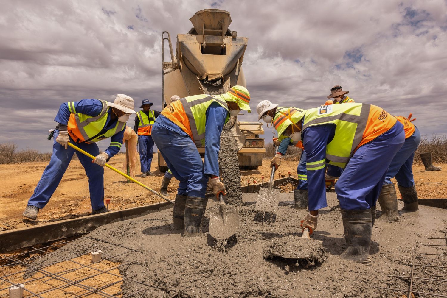 Concrete pouring activity at a construction site with workers and equipment in arid landscape.