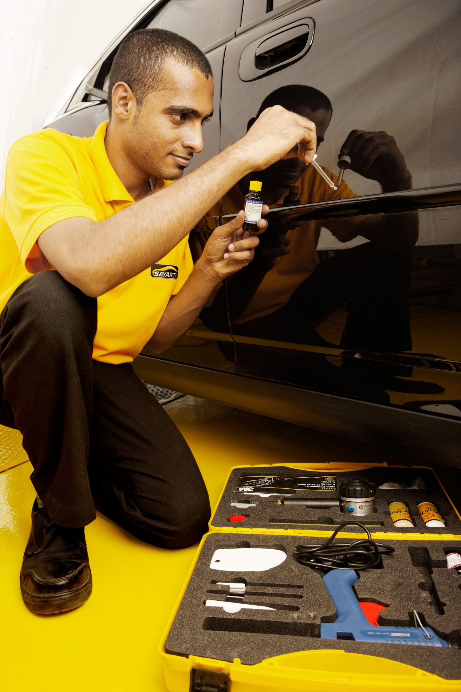 Mechanic in yellow uniform works with specialized diagnostic tools during car inspection.