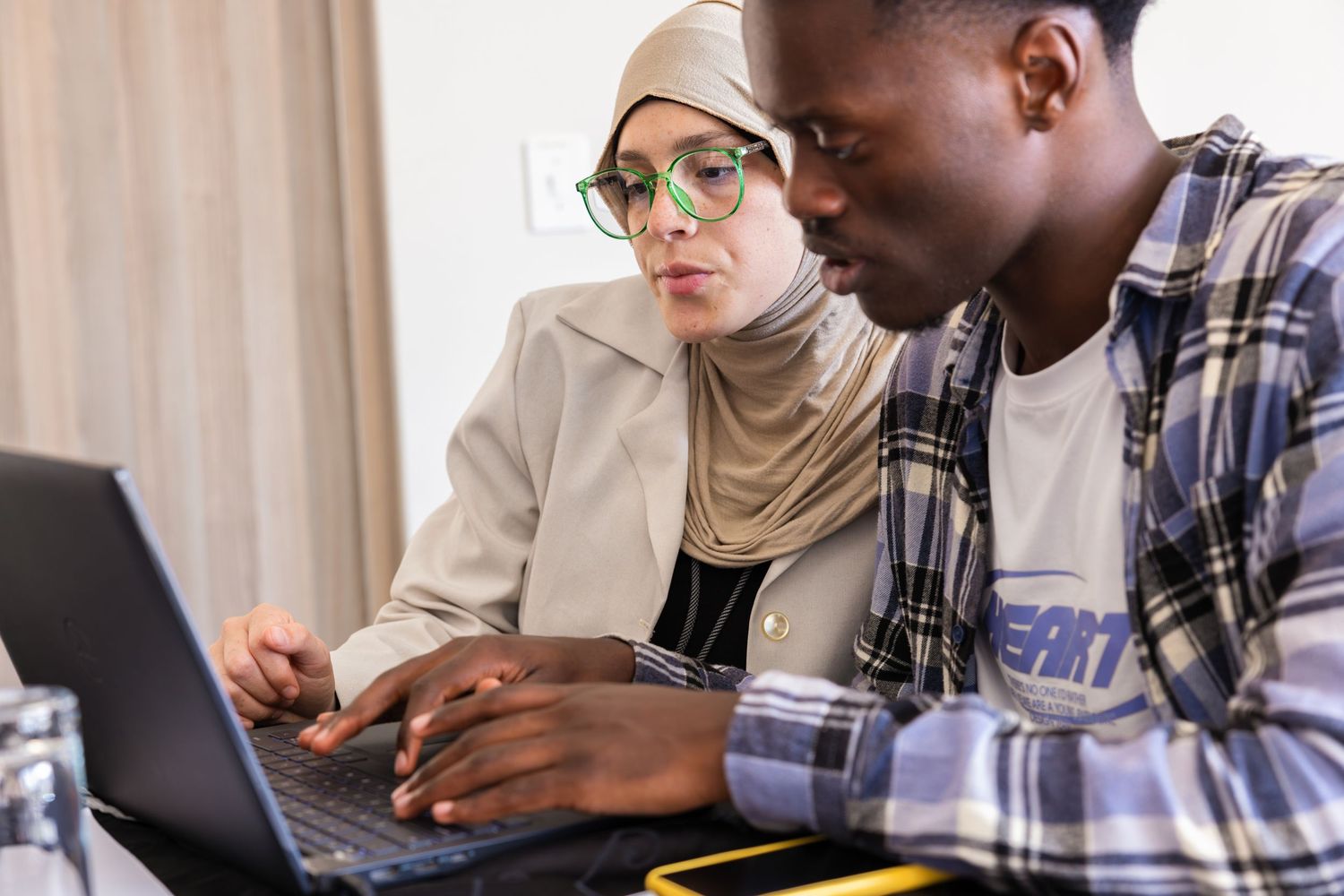 Two students collaborating on a laptop project in a modern study space.
