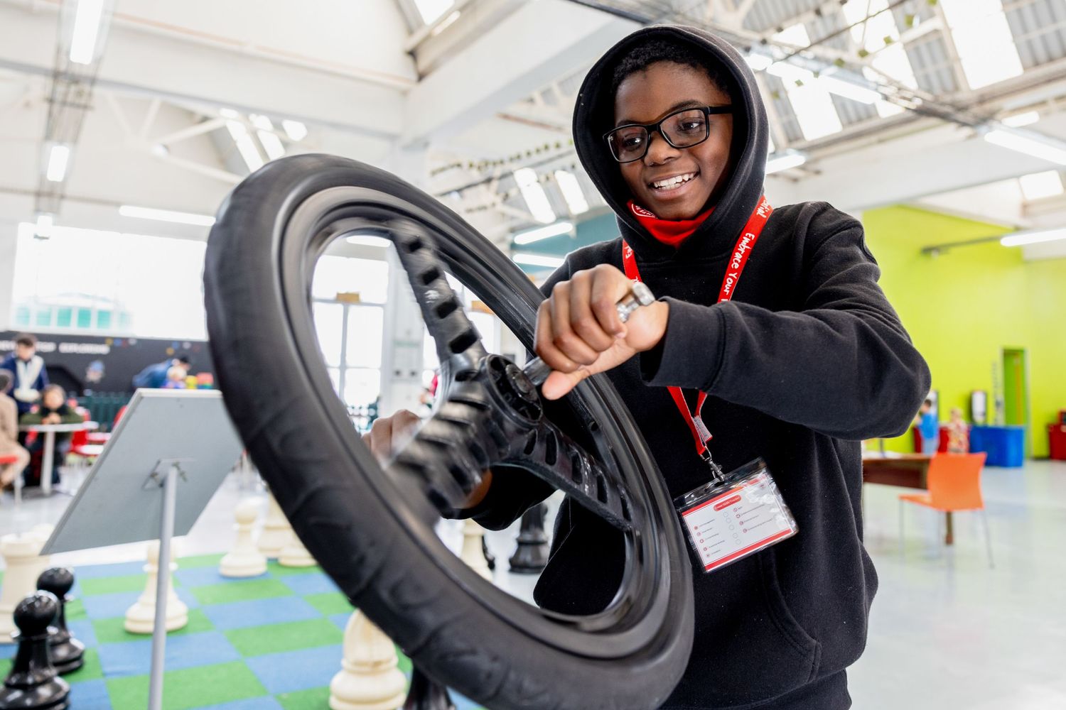 Person in black hoodie examining bicycle wheel in bright indoor space.