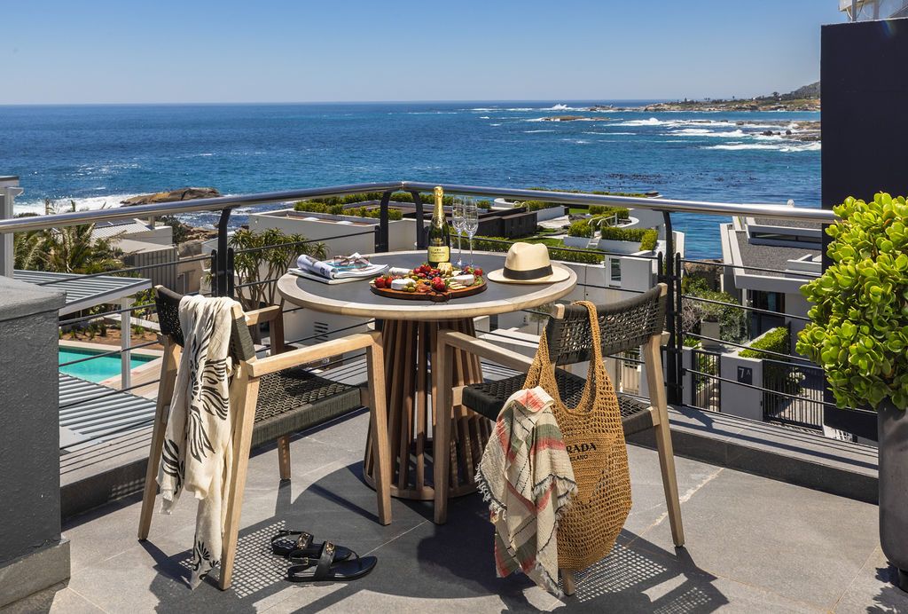 Coastal dining terrace with round wooden table and ocean views overlooking a scenic beach landscape.