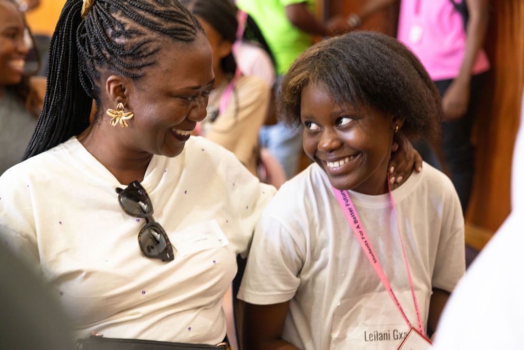 Two people share a joyful moment together while smiling and wearing light colored shirts at an indoor event.