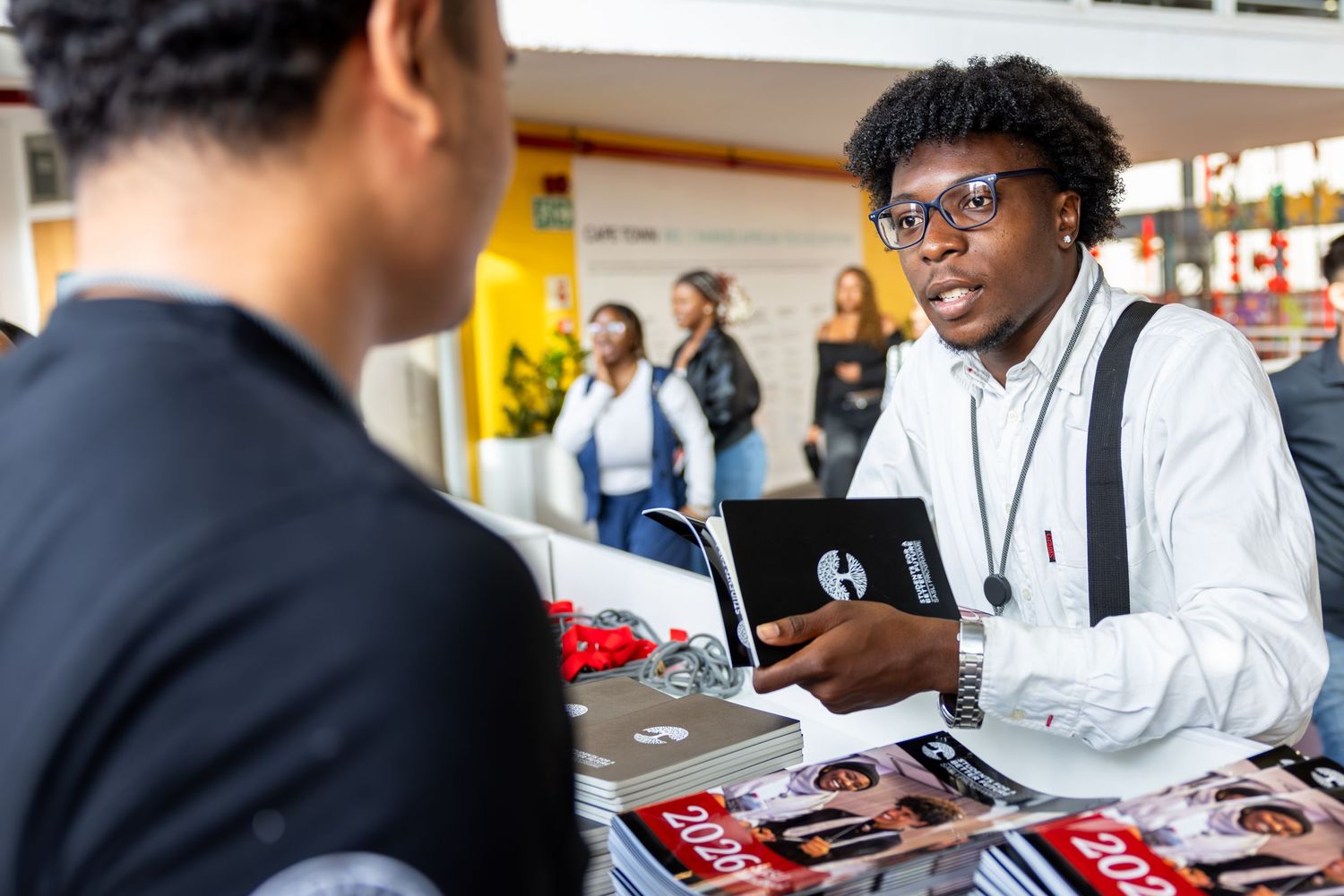 Students engage in discussion at a university career fair booth with promotional materials and handouts.