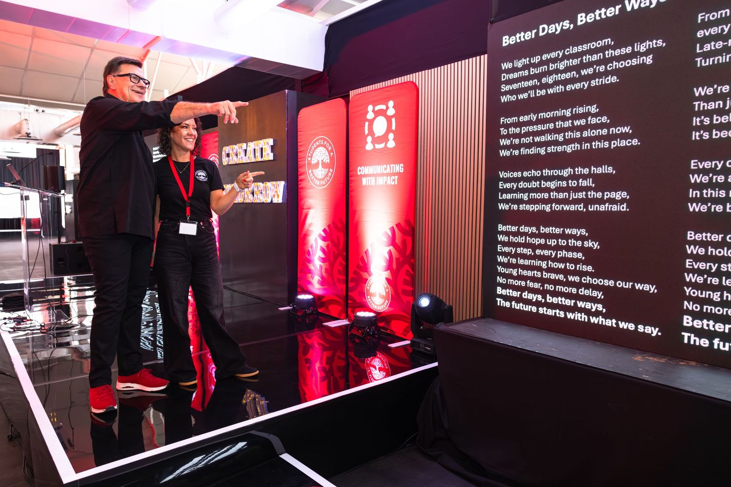 Dark conference room with red lighting displays digital presentation screens on stage.
