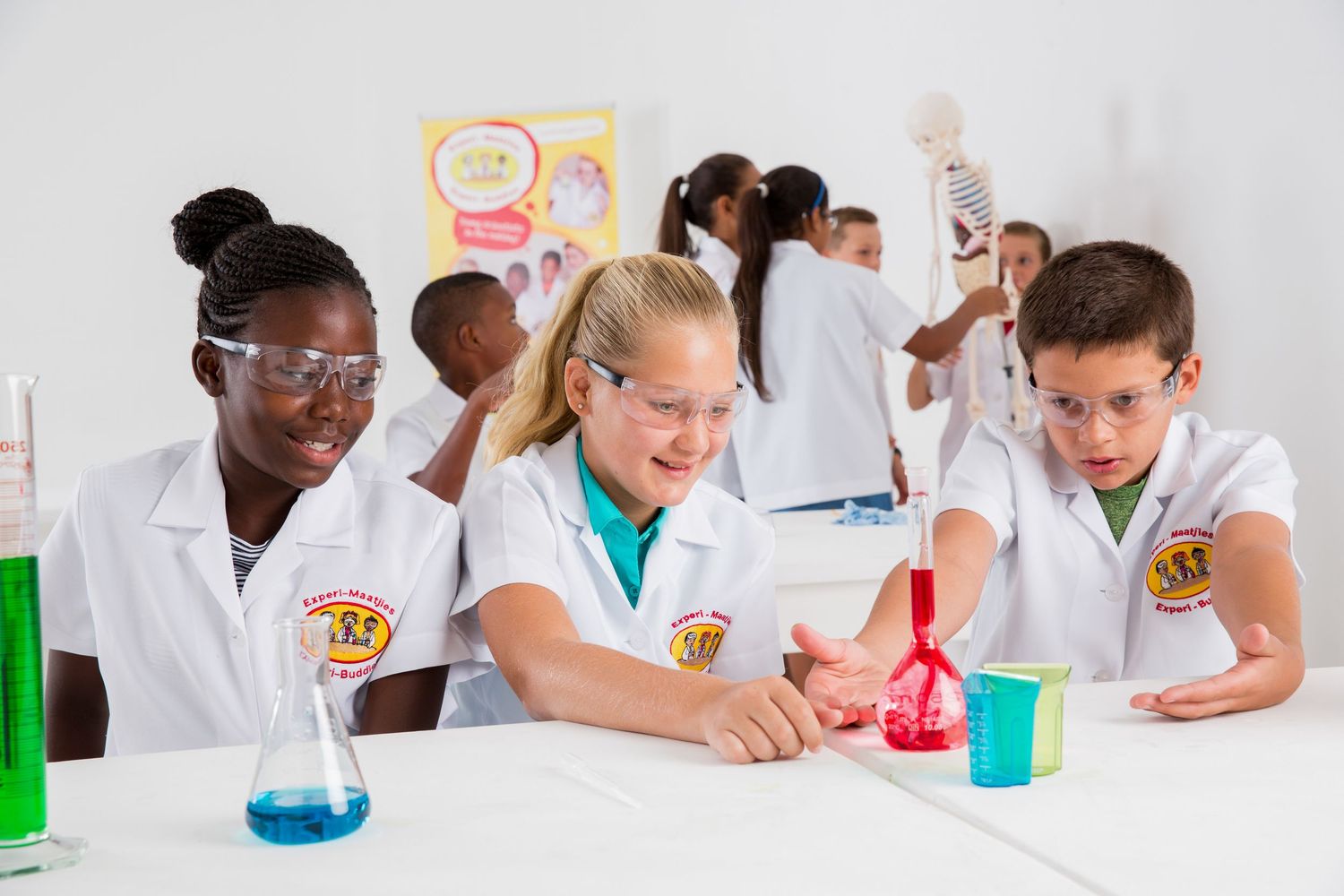 Students in safety goggles and lab coats work with colorful chemicals during science class.