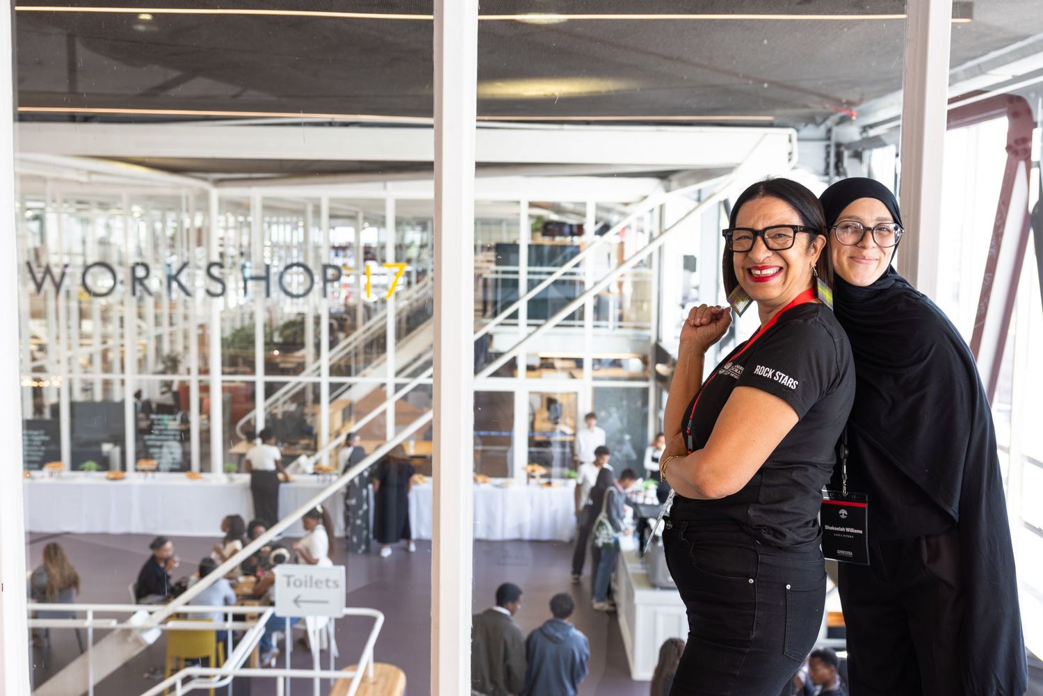 People in black attire gather for a workshop or event in a bright, modern space with glass walls.