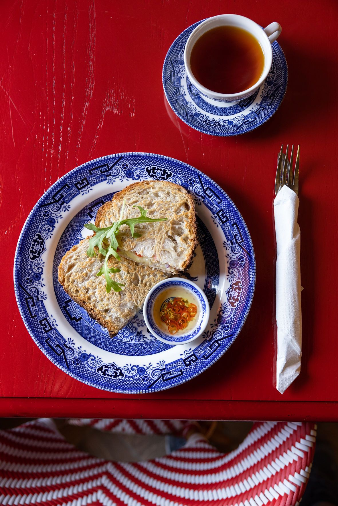 Blue and white willow pattern plates with sandwiches and tea on a red tablecloth.