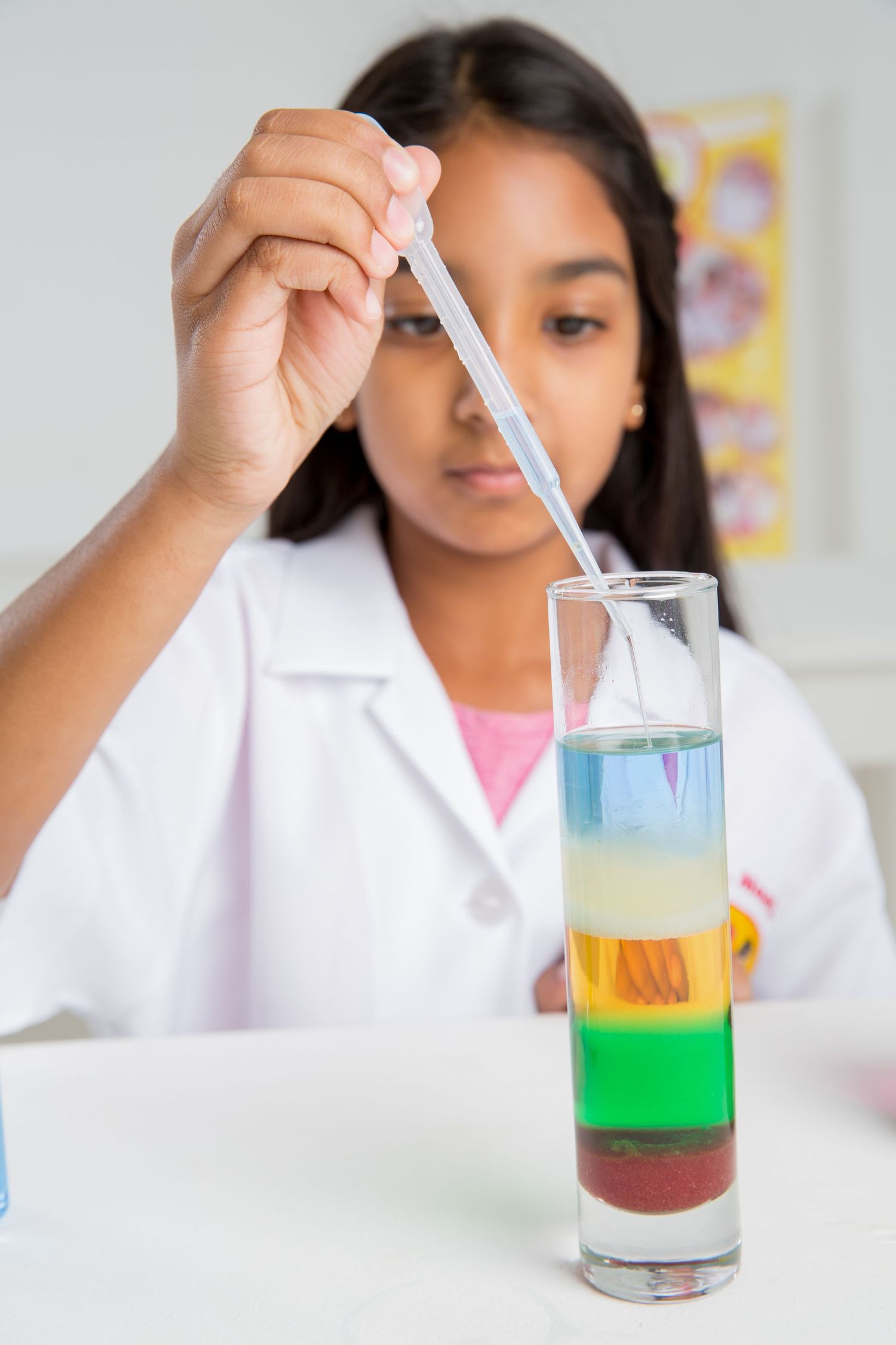 Student carefully pipettes liquid into layered rainbow density experiment in glass tube.