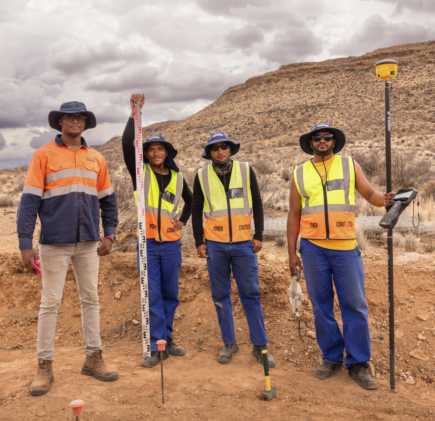 Construction workers with tools stand against desert mountain backdrop.