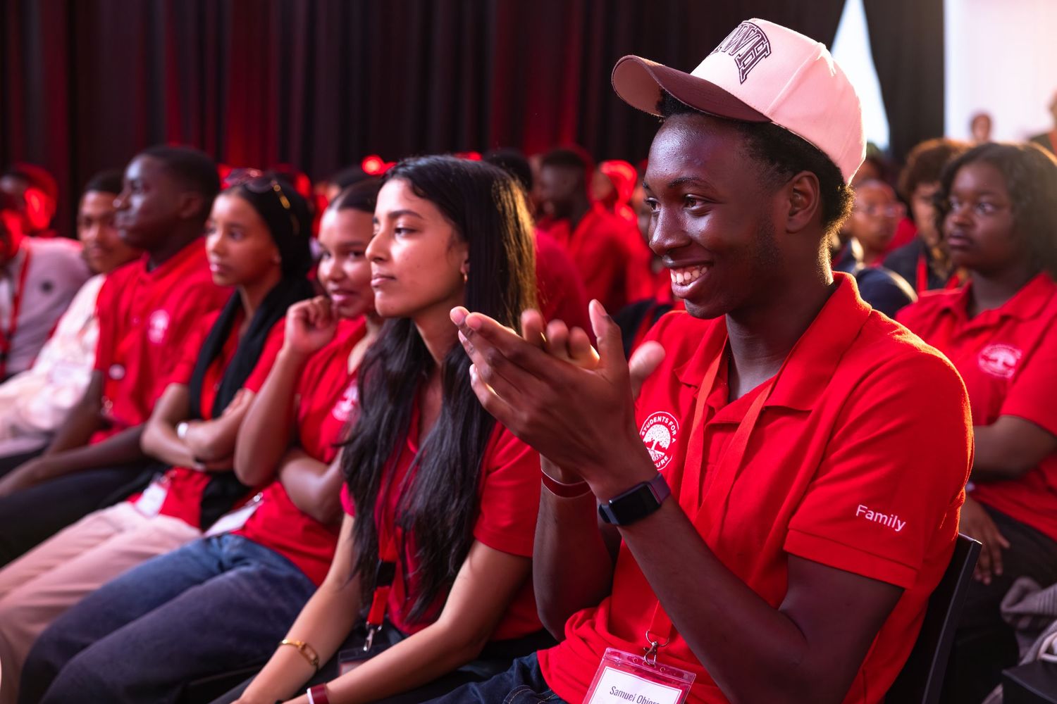 Audience members in red shirts watch attentively during a presentation event.