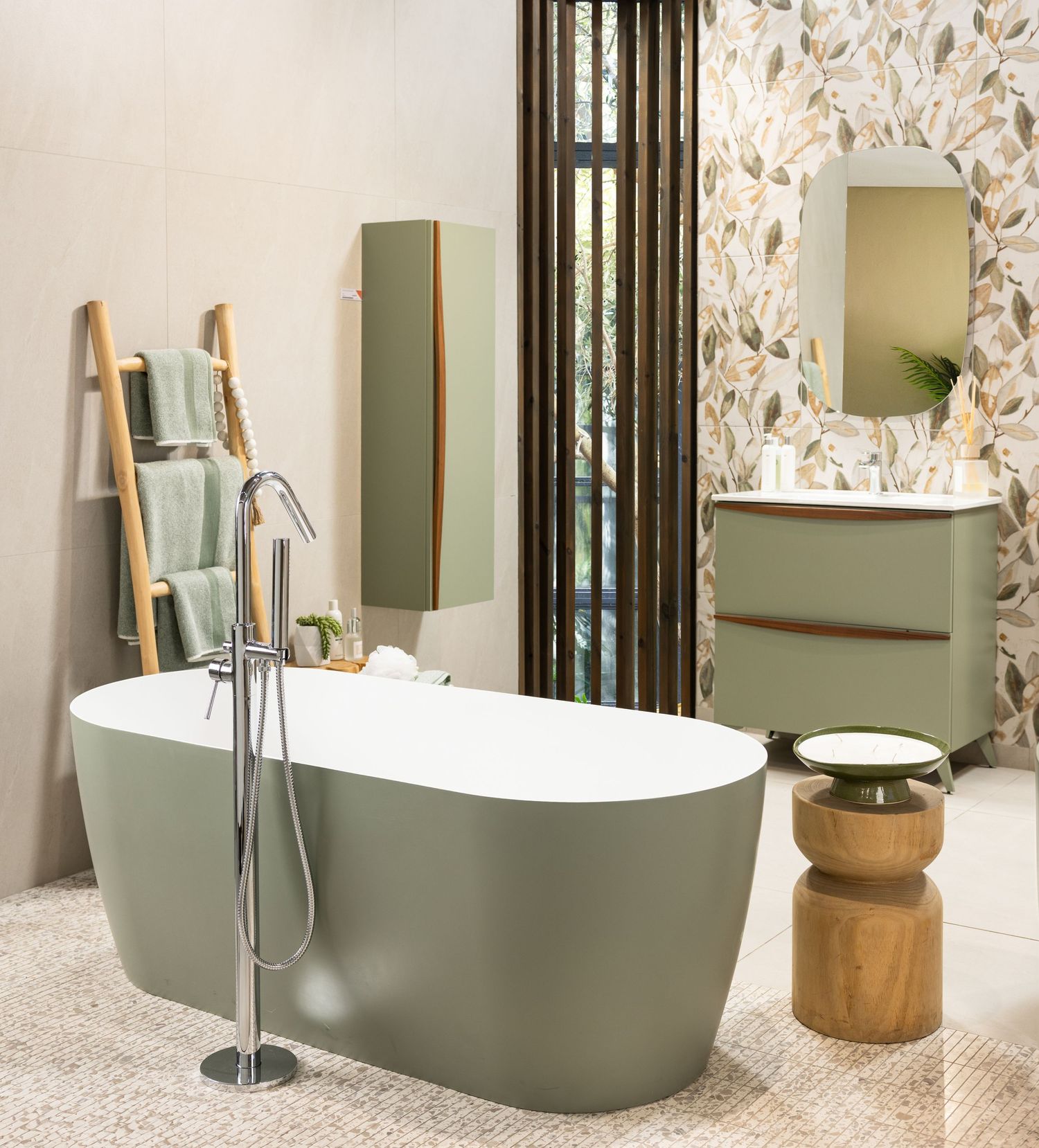 Modern bathroom featuring a sage green freestanding tub with wooden accents and floral wallpaper.