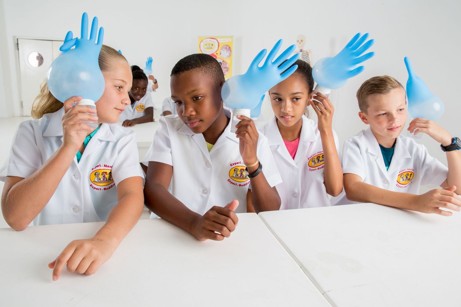 Students in lab coats wearing blue gloves examine scientific materials together at a white table.