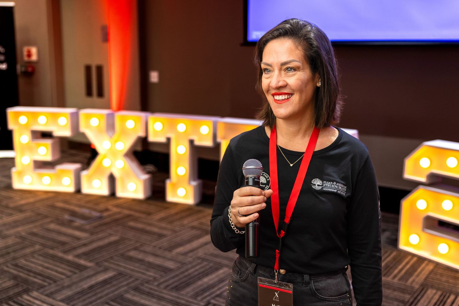 Conference attendees engage in discussions with illuminated signage in the background.